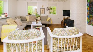 A cozy living room with a sofa, two white cribs, a TV, and a fireplace.