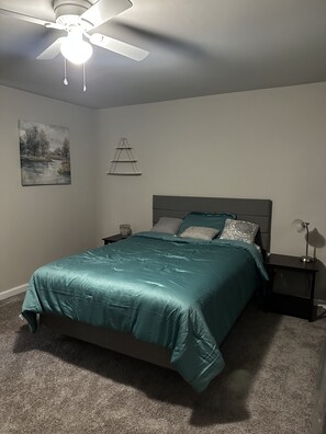 Une chambre à coucher comprenant un lit, des tables de chevet, un ventilateur de plafond, une étagère fixée au mur et un tableau.