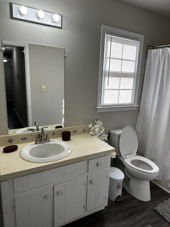 Une salle de bain équipée d’un lavabo, d’un miroir, de toilettes et d’une fenêtre avec des stores.