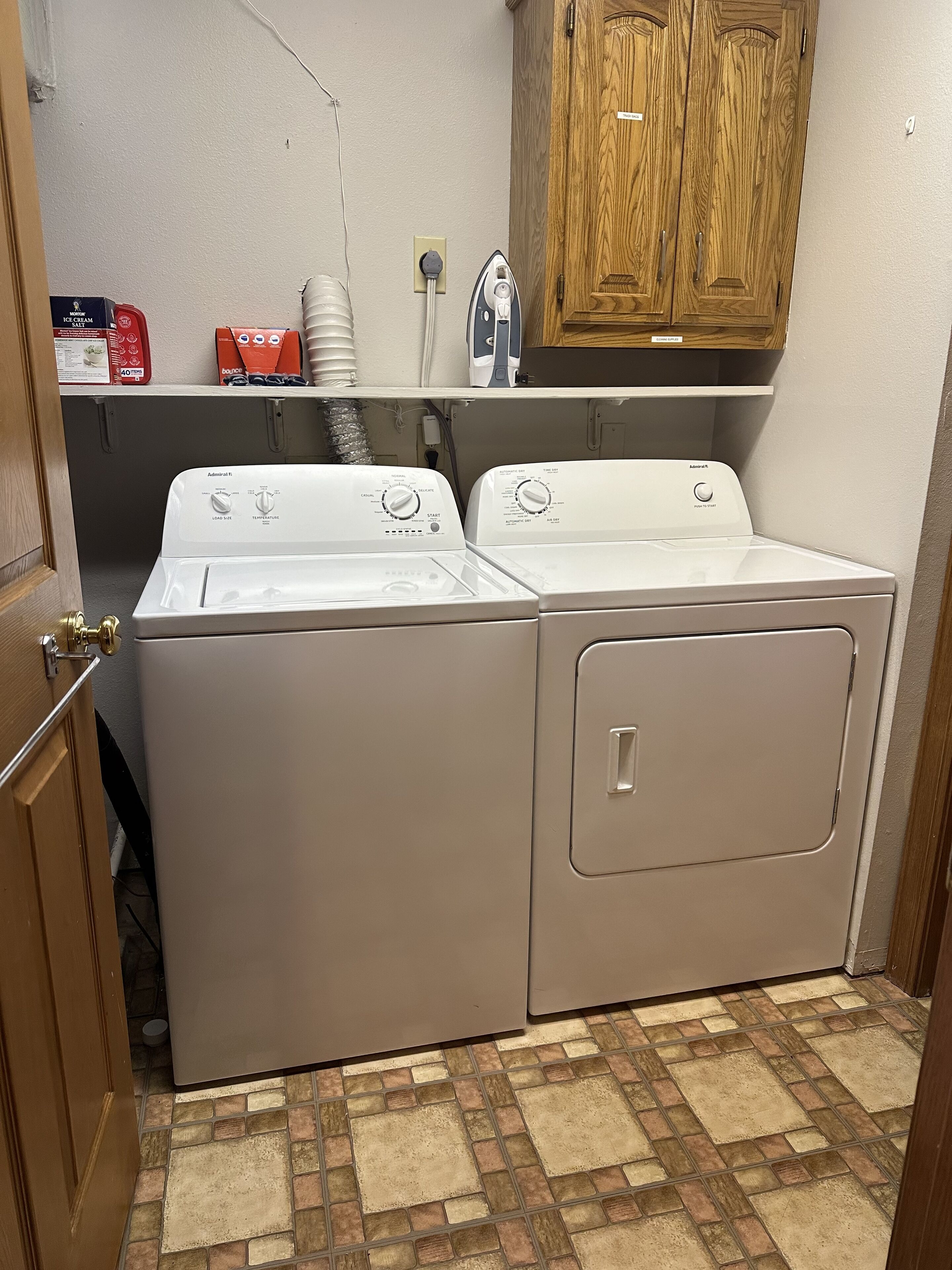 A laundry room with two front-loading washers and dryers, a wooden cabinet above, and a tiled floor.