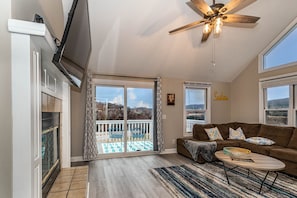 A spacious living room with a large window, a ceiling fan, and a fireplace.