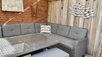 Eine Sitzecke mit grauer Websofa, einem Glastisch und einer kleinen Bank.