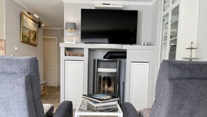 En moderne stue med grå sofaer, et fladskærms-tv, en pejs og et lille bord med bøger.