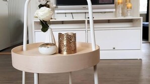 Ein modernes Wohnzimmer mit einem weißen TV-Schrank, einem weißen Sessel mit runder Holzsitze und einer Vase mit einer weißen Rose.