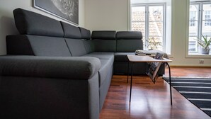 A modern living room with a sectional sofa, a small table, and a large window providing a view of the cityscape. - In Heart of Stavanger BnB with Billiard & Sauna (Stavanger)