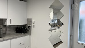 Cozinha moderna com armários brancos, uma cafeteira preta e um espelho refletindo o ambiente.