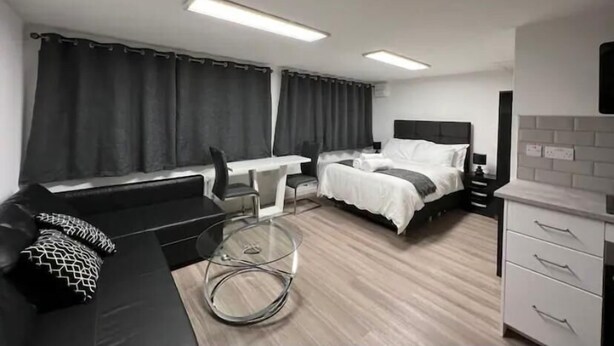 Quarto de hotel moderno com cama, sofá, mesa de jantar e cozinha.