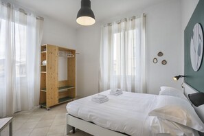 A bedroom with a bed, a wooden wardrobe, a desk, and a wall-mounted lamp.