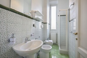 A bathroom with a large sink, two toilets, a shower, and a window providing natural light.