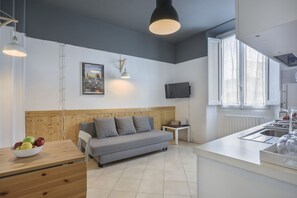 A modern kitchen with a grey sofa, wooden accents, and a TV mounted on the wall.