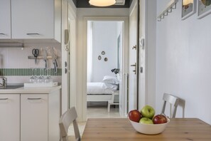 A kitchen with white cabinets, a sink, and a bowl of fruit on a table.