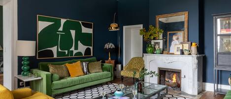 A living room with a green sofa, yellow armchairs, a glass coffee table, and a fireplace.
