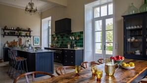 A kitchen with a wooden dining table, bar stools, a large island, and a dark cabinet with glass doors. - Refurbished Chateau, Sleeps 20 with Luxury Pool (Labarthe)