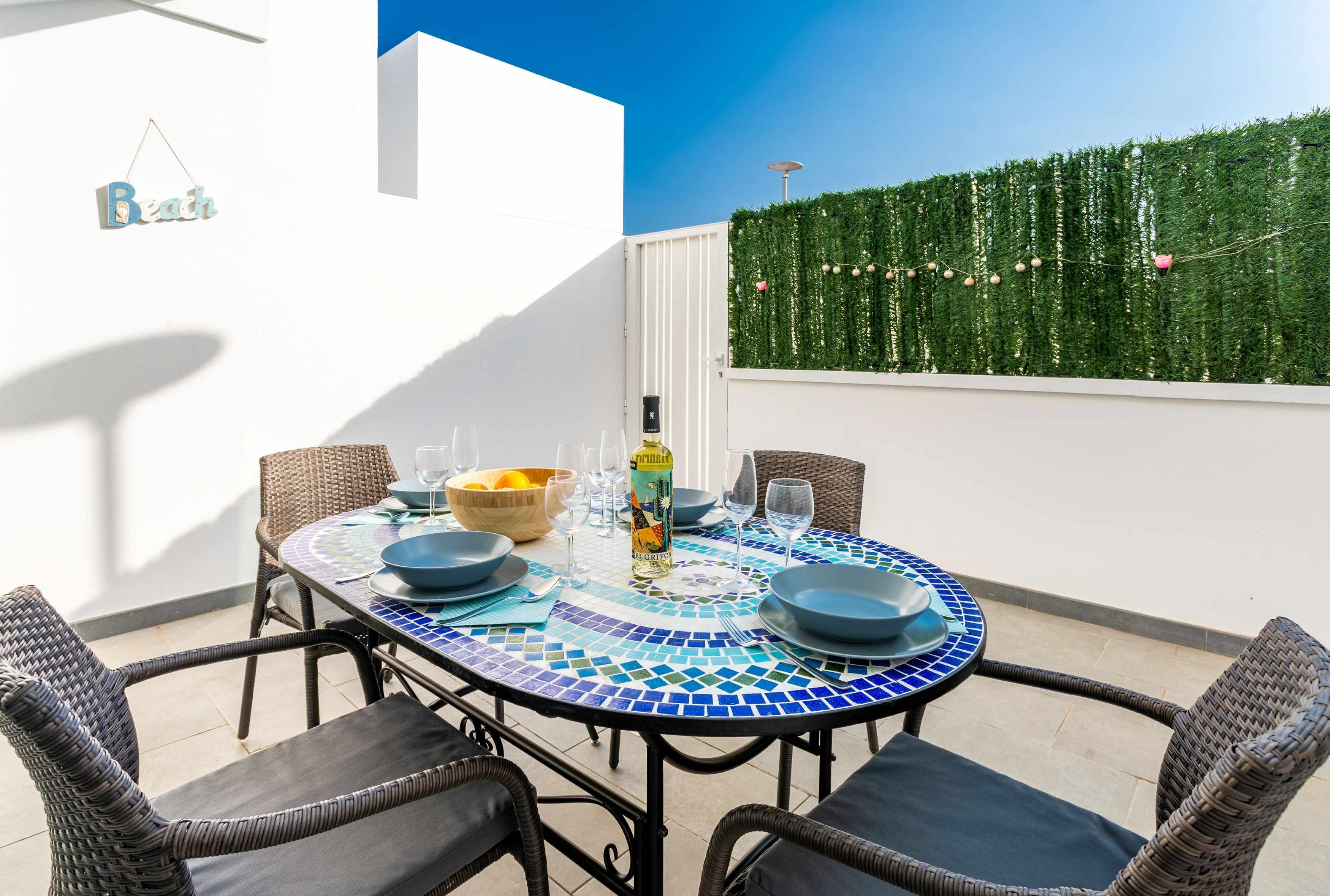 Un espace de restauration en plein air avec une table ronde, des chaises en osier et une nappe à carreaux bleus et blancs.
