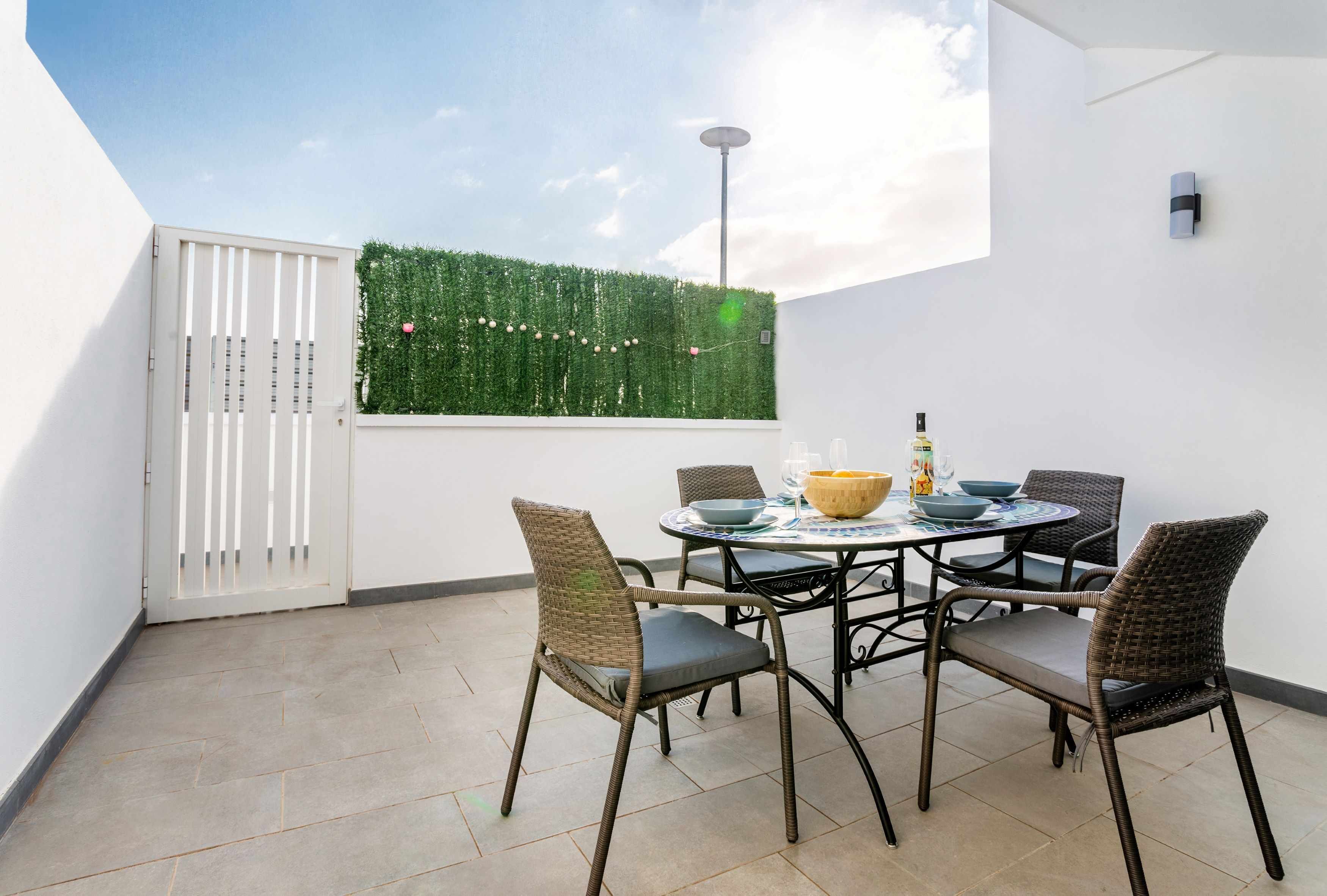 A patio with a round table, wicker chairs, and a decorative wall.