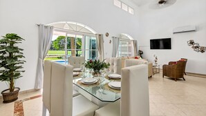 A spacious dining area with a glass table, white chairs, and a view of a swimming pool. - Beautiful Villa in Cocotal Golf Punta Cana (Punta Cana)
