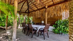 An outdoor dining area with a thatched roof, wooden tables, and chairs, surrounded by tropical plants. - Beautiful Villa in Cocotal Golf Punta Cana (Punta Cana)