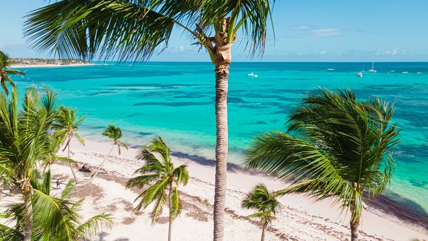 A beach with clear turquoise water, palm trees, and boats in the distance. - Beautiful Villa in Cocotal Golf Punta Cana (Punta Cana)
