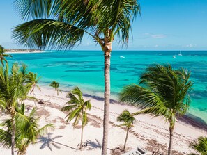 Uma praia com águas turquesa cristalinas, palmeiras e barcos ao longe.