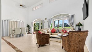 A spacious living room with a sofa, two wicker chairs, a coffee table, and a dining area with chairs and a table. - Beautiful Villa in Cocotal Golf Punta Cana (Punta Cana)