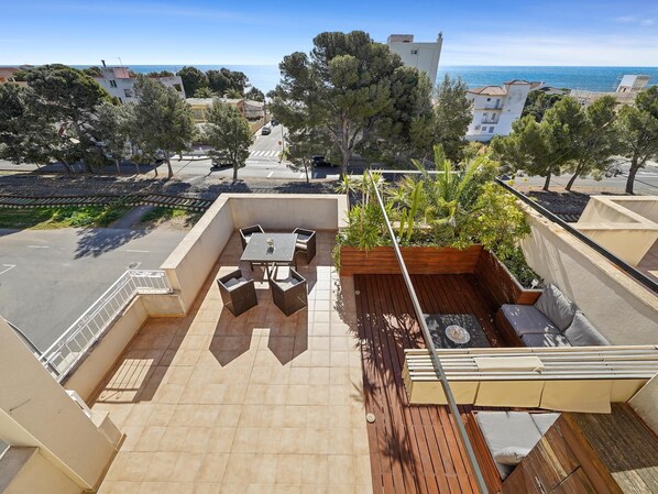 Terraço no telhado com mesa e cadeiras, um espaço de estar pequeno e vista para o mar e edifícios ao redor.