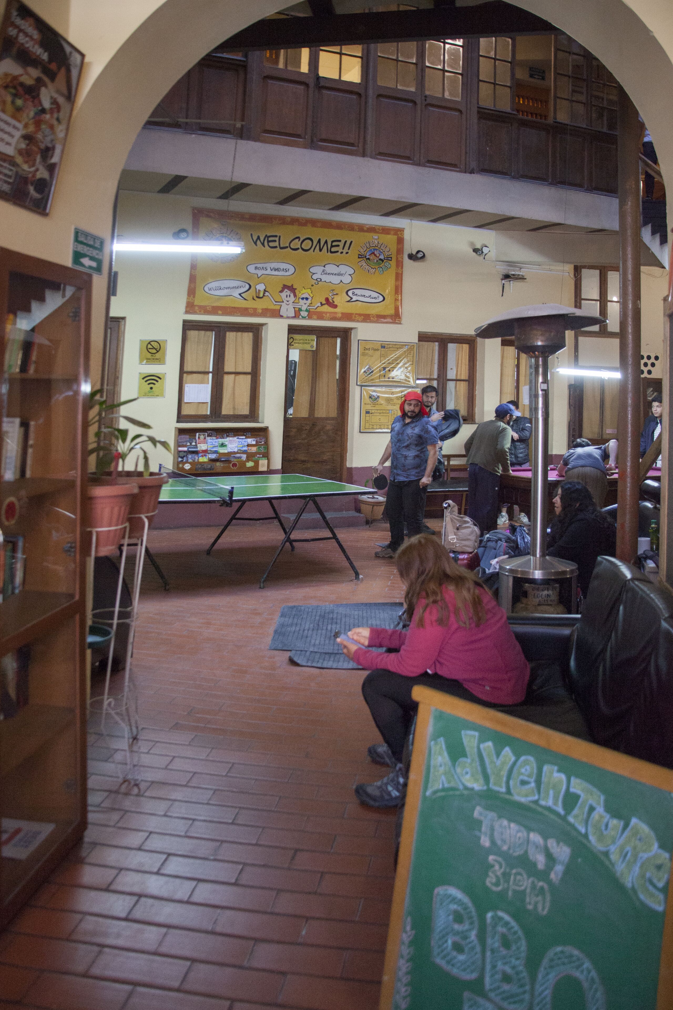 Amplio espacio interior con mesa de ping pong, un cartel de pizarra anunciando un evento y un techo alto con vigas de madera.