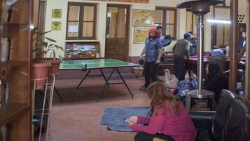 A spacious indoor area with a ping pong table, a chalkboard sign advertising an event, and a high ceiling with wooden beams.