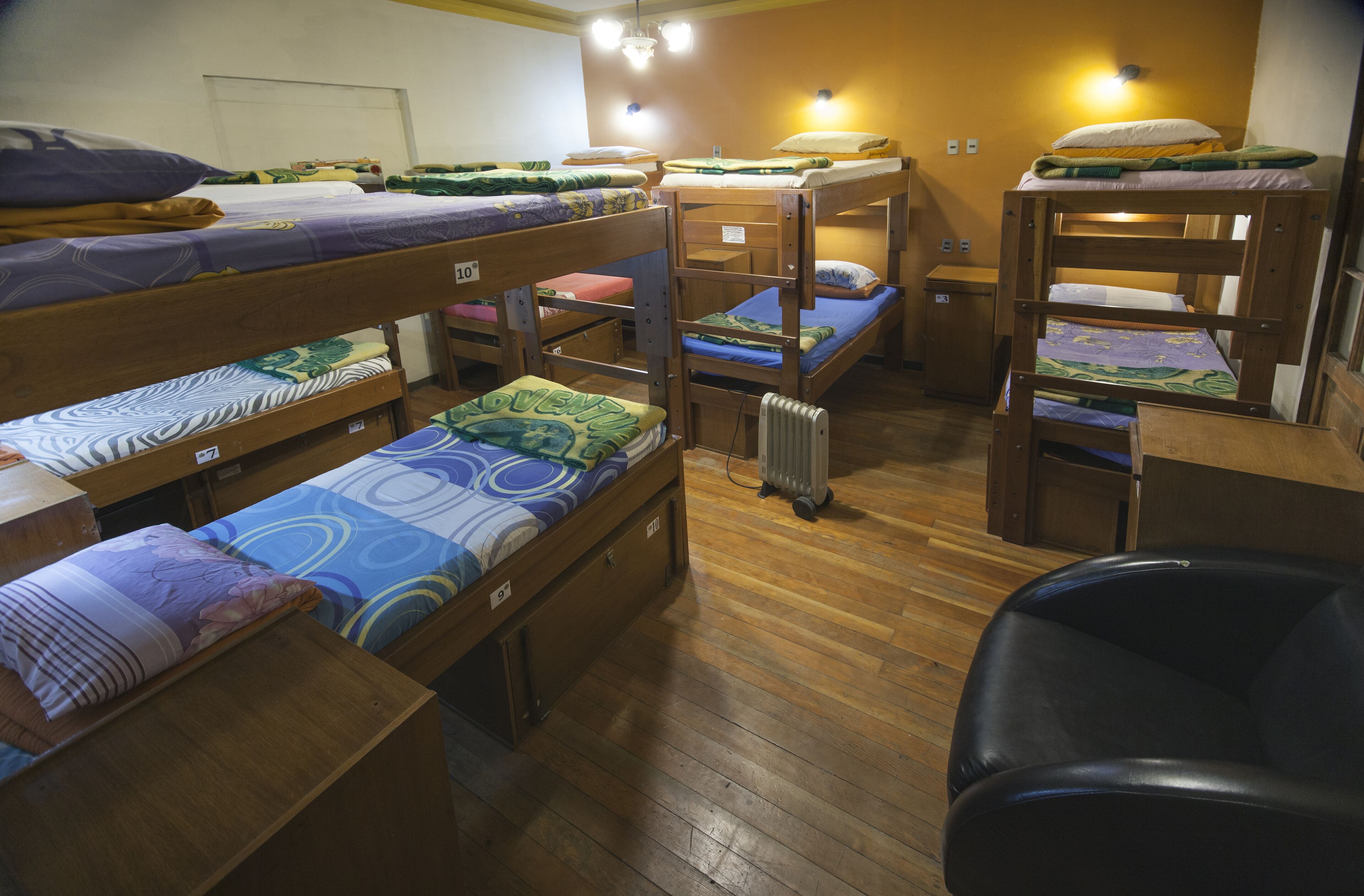 Een slaapzaal met stapelbedden, houten vloeren en een radiator.