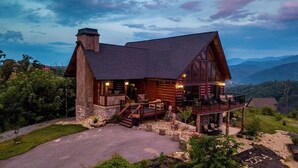 A log cabin with a stone chimney, a deck, and a view of the surrounding mountains.