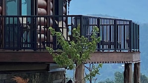 A log cabin with a balcony, a tree in the foreground, and a bear in the background.