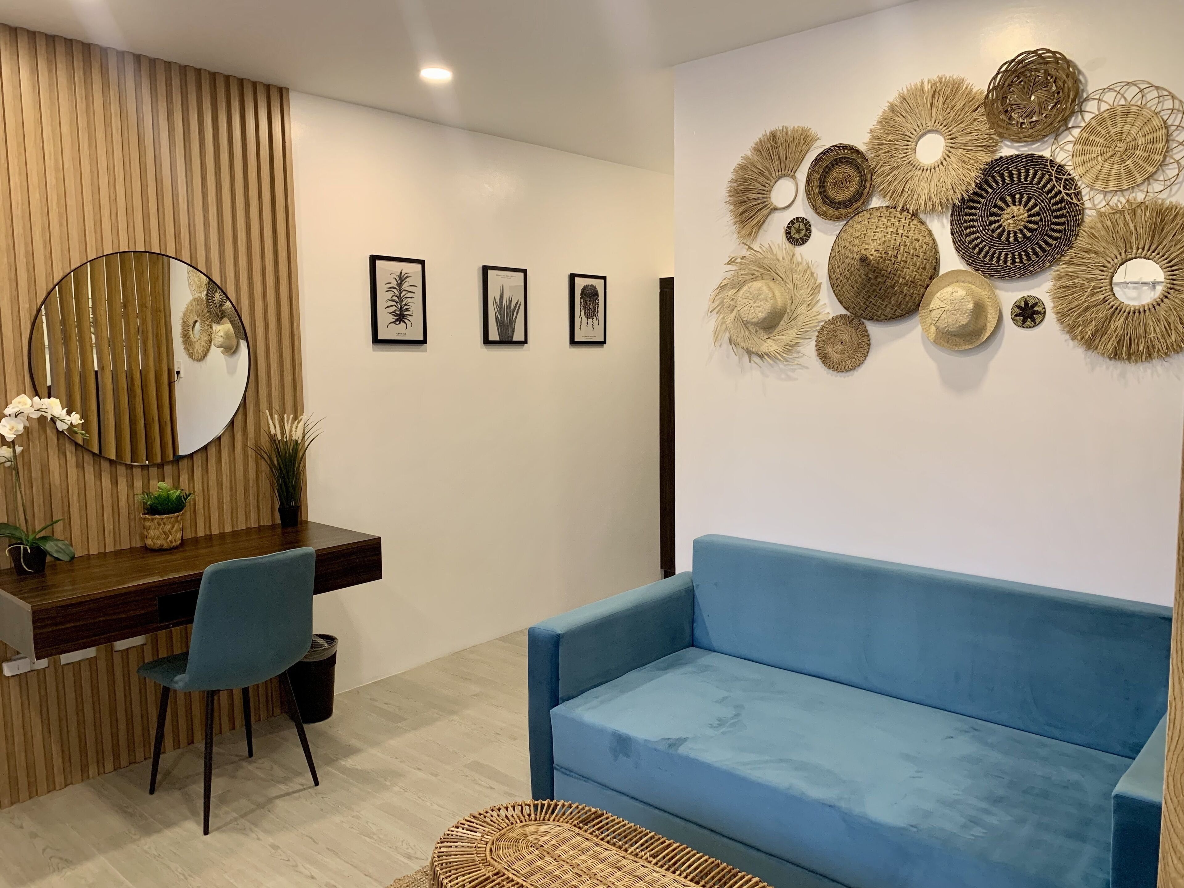 A modern living room with a blue sofa, a wooden desk with a chair, a round mirror, and wall-mounted decorative items.