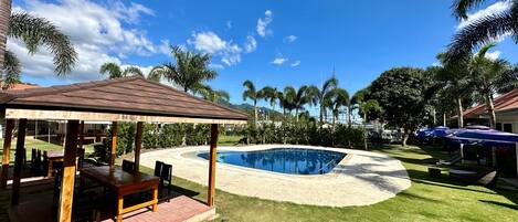 A pool area with a gazebo, palm trees, and a clear blue sky.