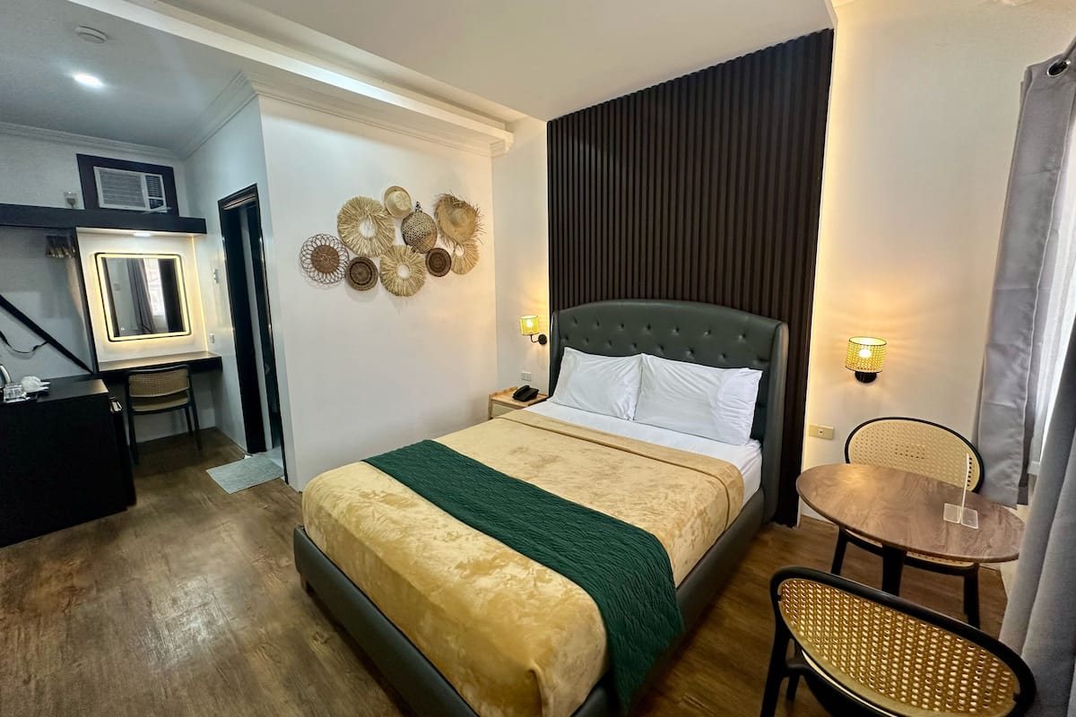 Een hotelkamer met een bed, nachtkastje, stoel en een tafeltje met een lamp.