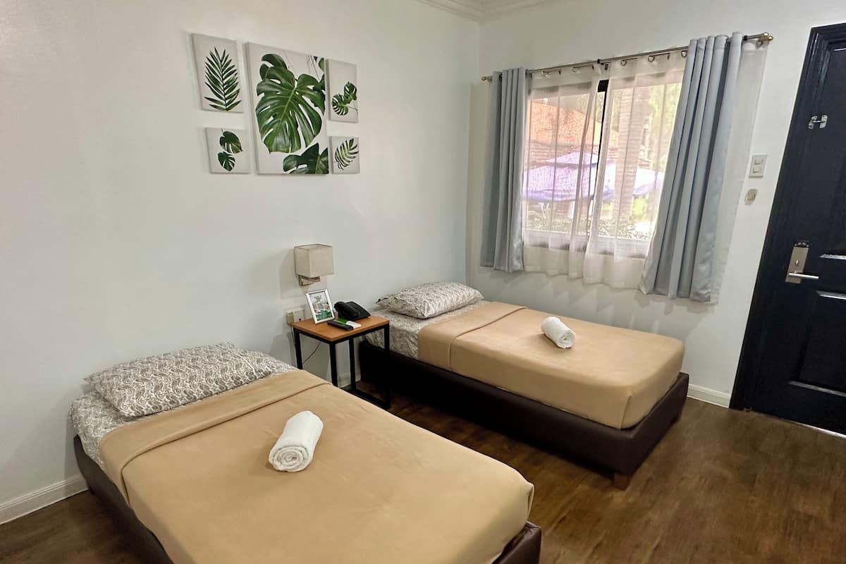 Een hotelkamer met twee bedden, een kleine tafel met een lamp, een fotolijst en een raam met gordijnen.