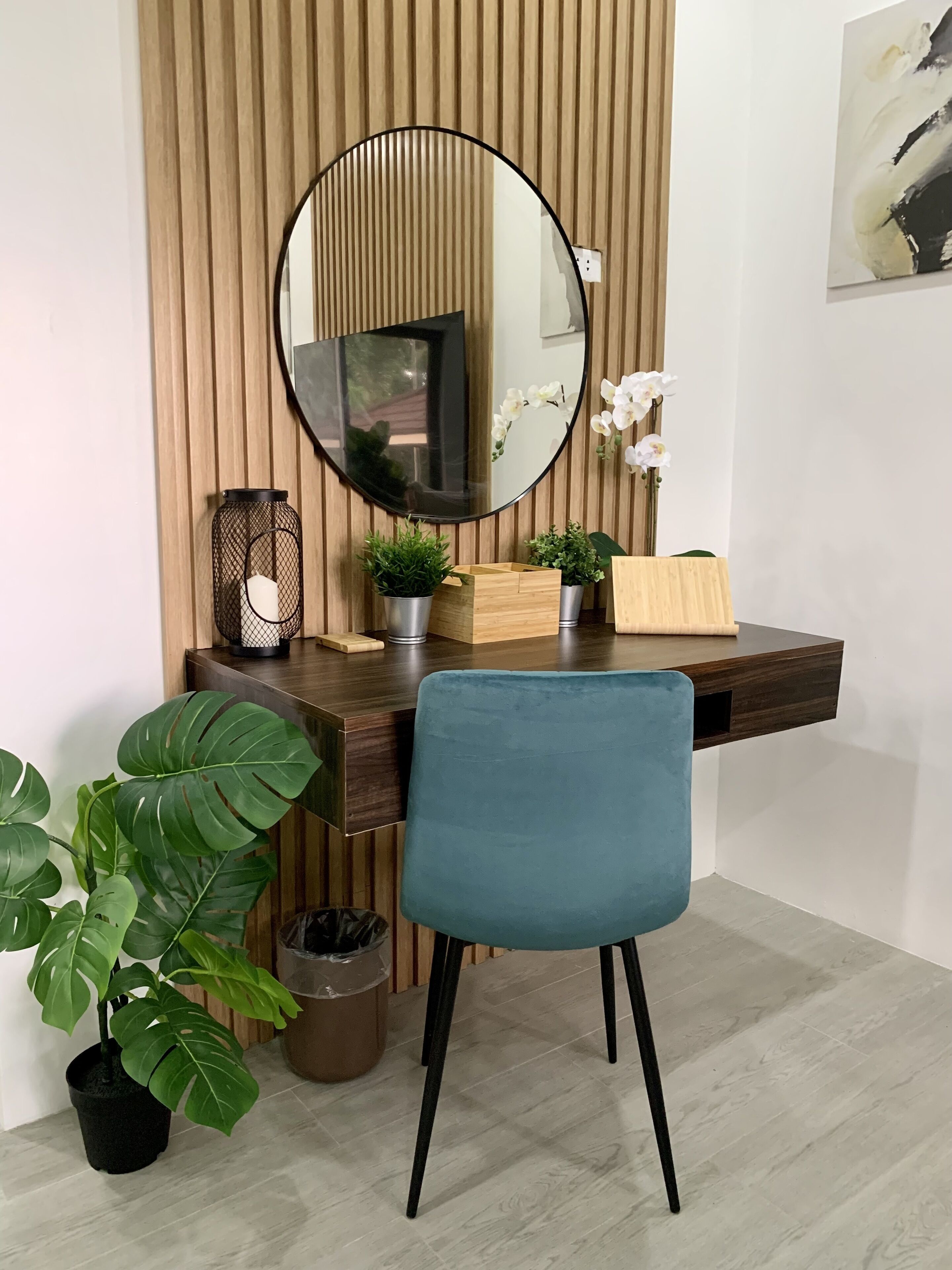 A modern desk with a round mirror, a blue chair, and potted plants.