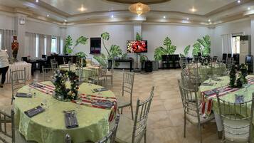 A banquet hall with round tables, chairs, and a Christmas tree.