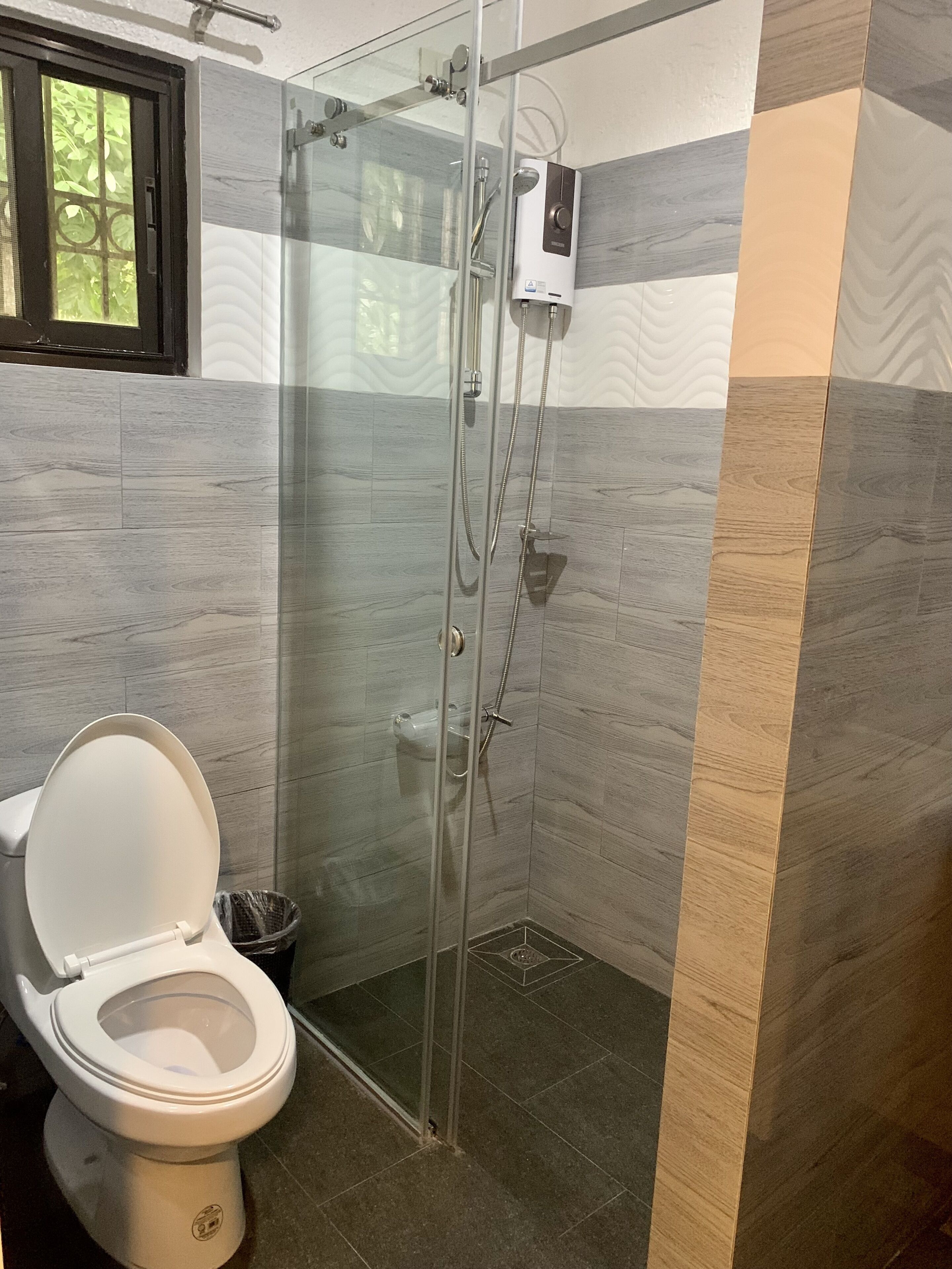 A modern bathroom with a glass-enclosed shower, a toilet, and a wall-mounted heater.