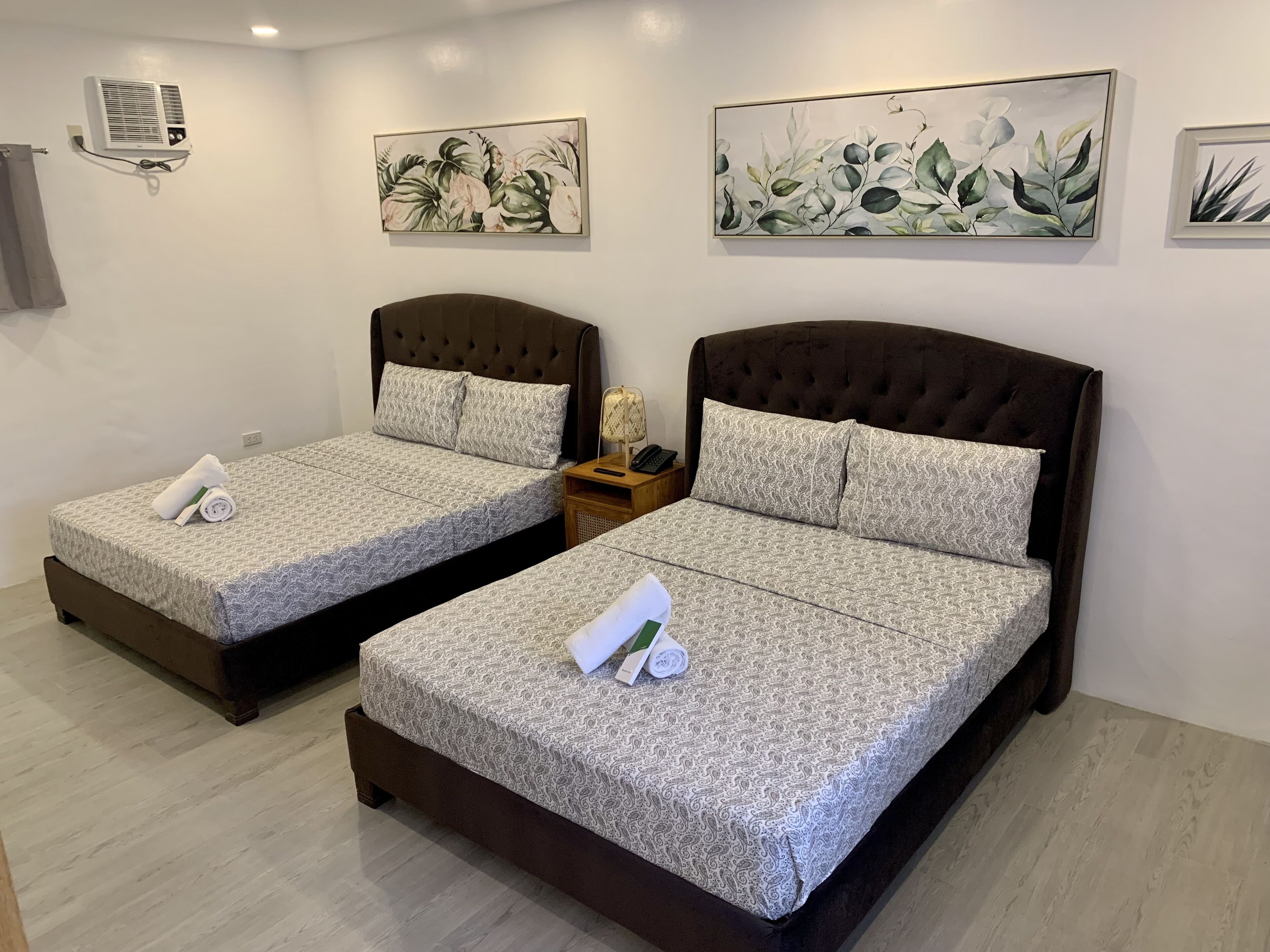 Two twin beds with matching headboards and patterned bedding, a bedside table with a lamp, and wall-mounted artwork.