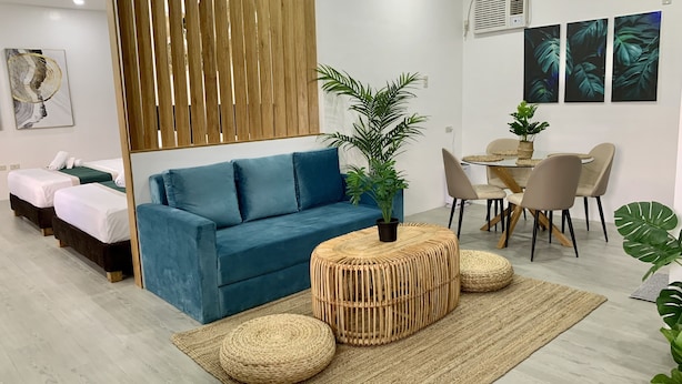 A modern hotel room with a blue sofa, a dining area with a round table and chairs, and a large potted plant.