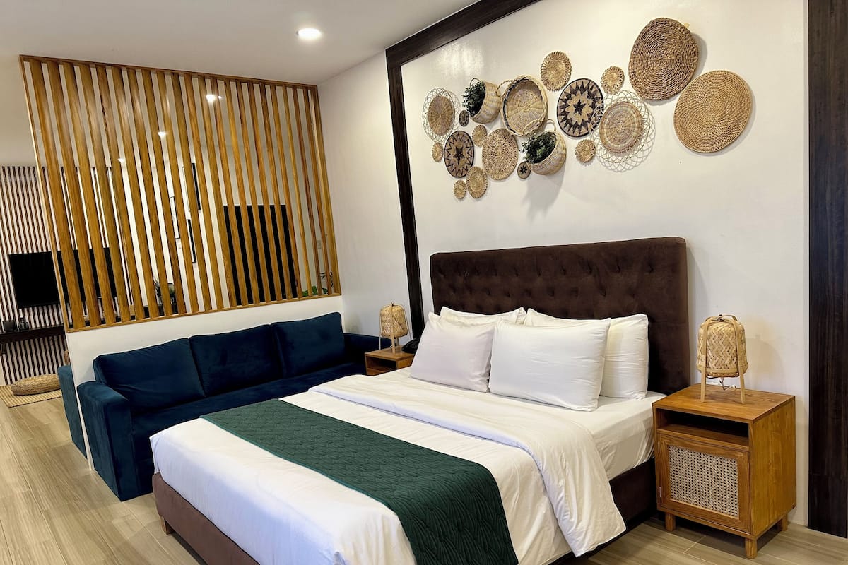 Een moderne slaapkamer met een groot bed, een donkerblauwe bank, een houten hoofdeinde en een wand versierd met gevlochten manden.