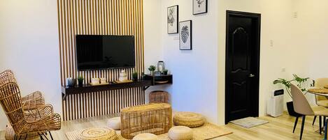 A modern living room with a flat-screen TV, wicker furniture, and a black door.