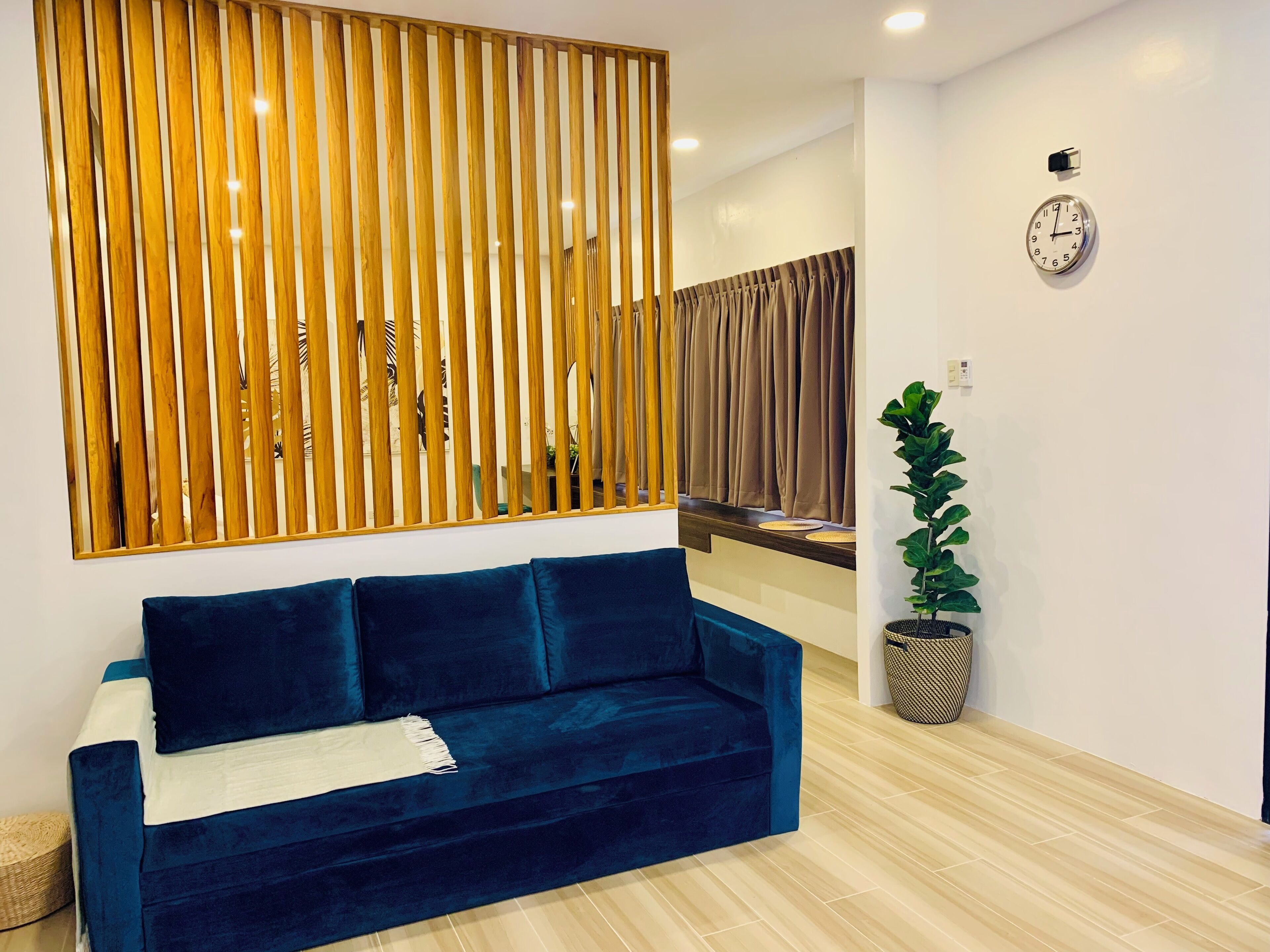 A modern living room with a dark blue sofa, wooden slat partition, a round clock, and a potted plant.