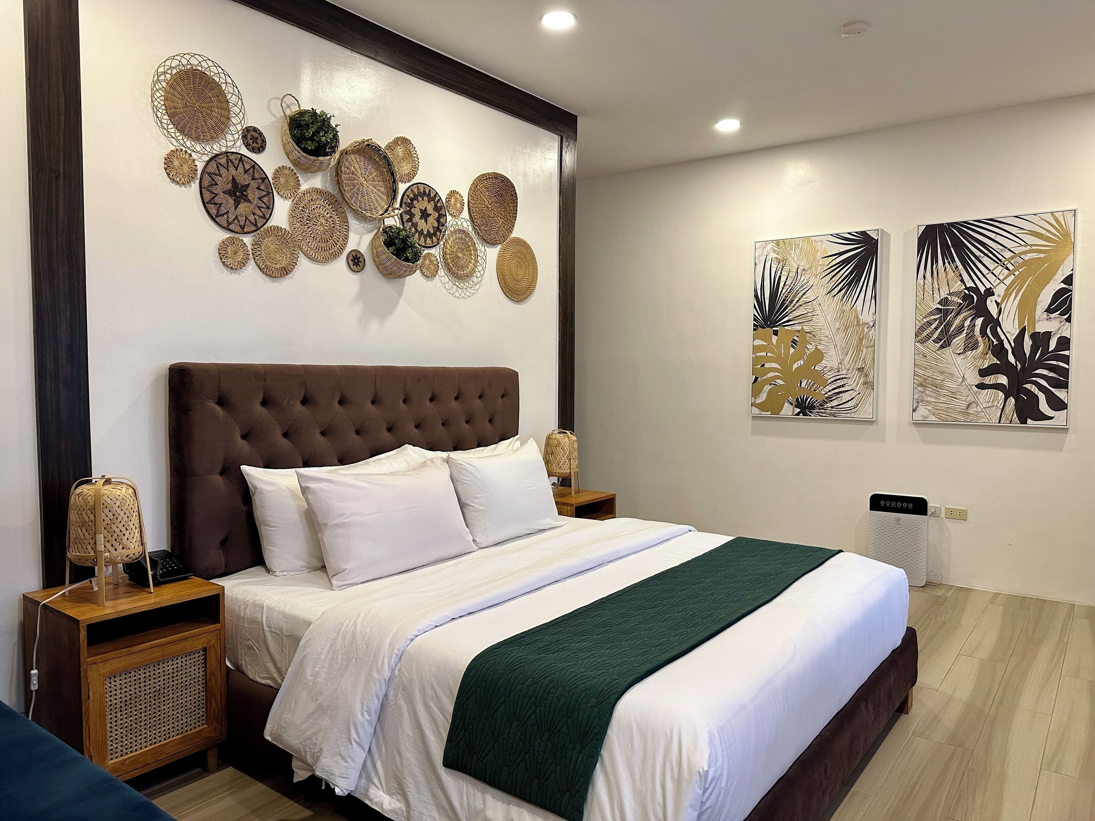 A neatly made bed with a tufted headboard, white bedding, and a green throw blanket. There are two bedside tables with lamps and a wall-mounted decorative item above the bed.