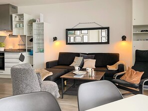 Een moderne woonkamer met een bank, fauteuils, een salontafel en een eettafel. Er is een keuken met kasten en een werkblad te zien.