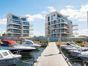 A marina with modern apartment buildings, docked boats, and a wooden walkway.