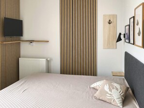 A bedroom with a bed, a wall-mounted TV, a radiator, and a wooden panel wall. - Sandpiper (Wendtorf)