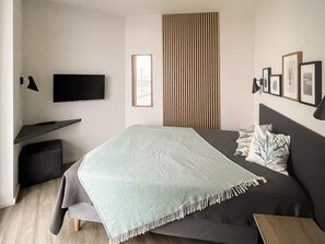 Een moderne slaapkamer met een bed, een bureau, een televisie en ingelijste foto's aan de muur.