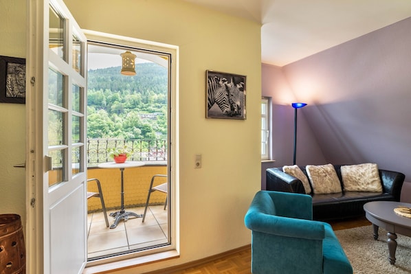 A room with a balcony, a sofa, a chair, and a table.
