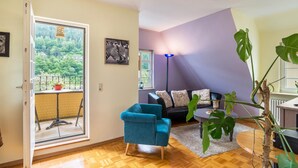 A living room with a sofa, a blue chair, a large plant, and a view through a glass door.