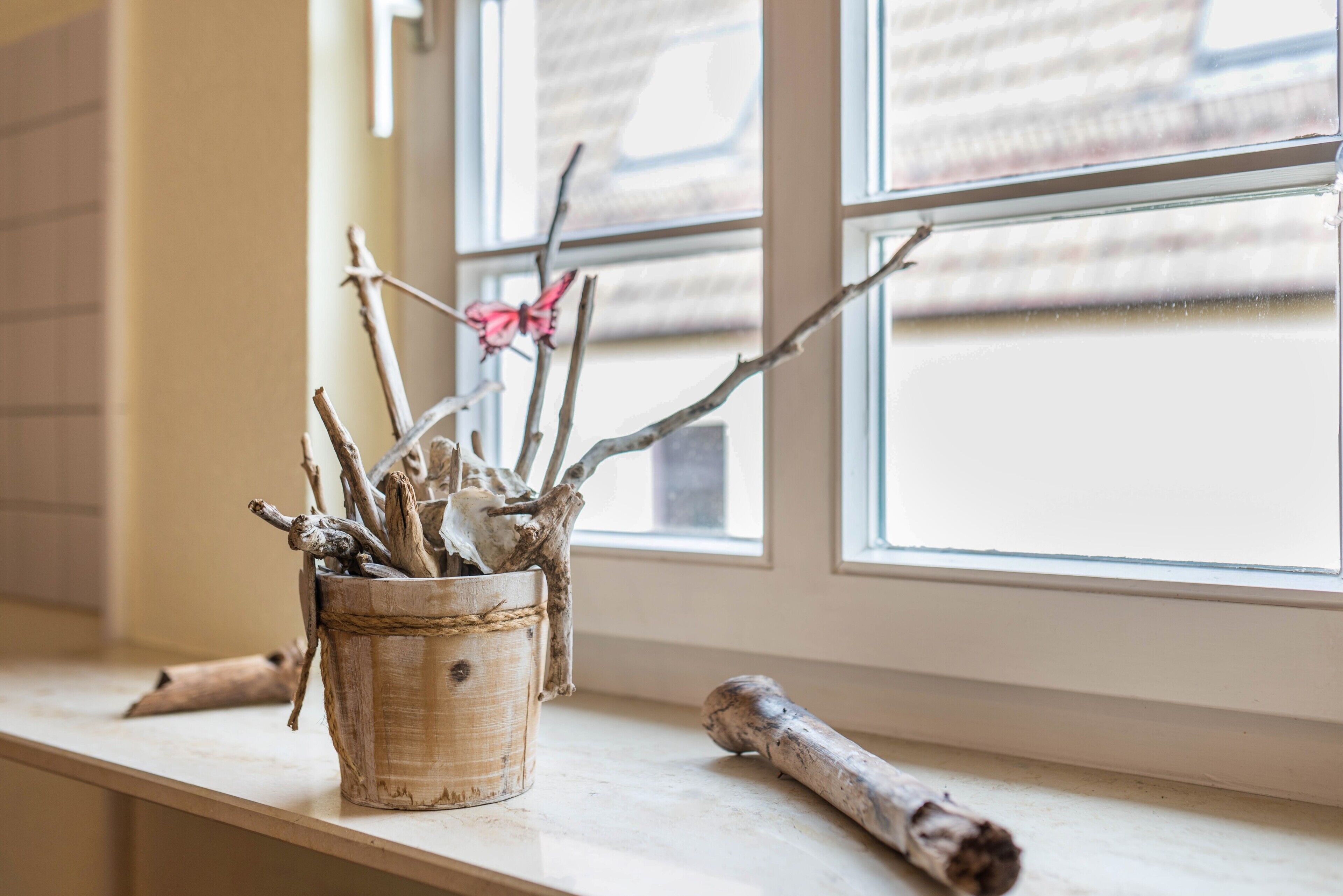Un rustico vaso di legno con rami e una decorazione a forma di farfalla su un davanzale.